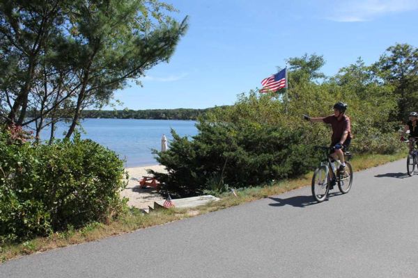 Photograph of man biking and pointing a finger at long pond in harwich while passing it 